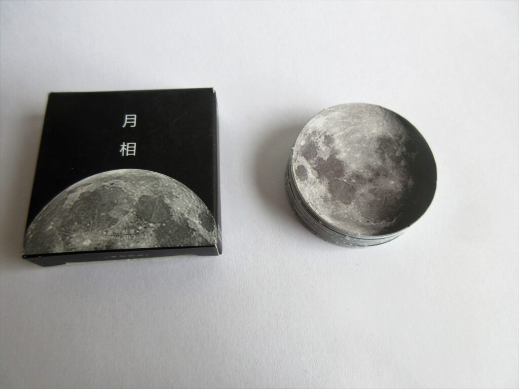 Moon stickers stacked over one another, along with a box containing a moon design